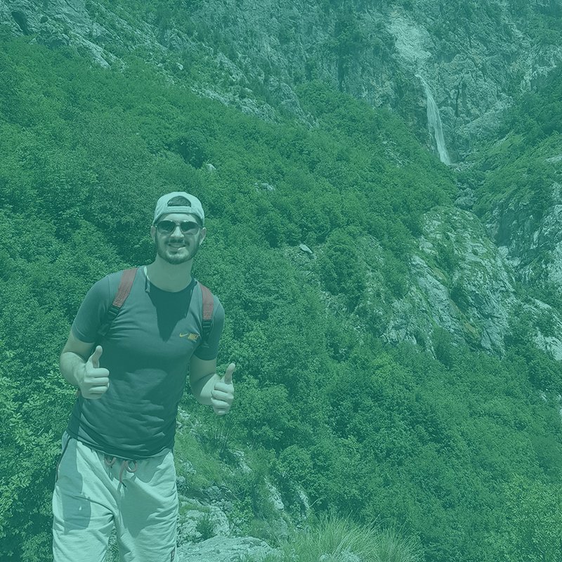 Man with baseball cap hiking in front of a mountain backdrop.