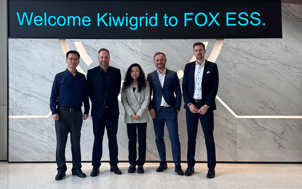 4 men and a woman in business attire stand in a reception hall with a monitor that reads “Welcome Kiwigrid to FOX ESS”