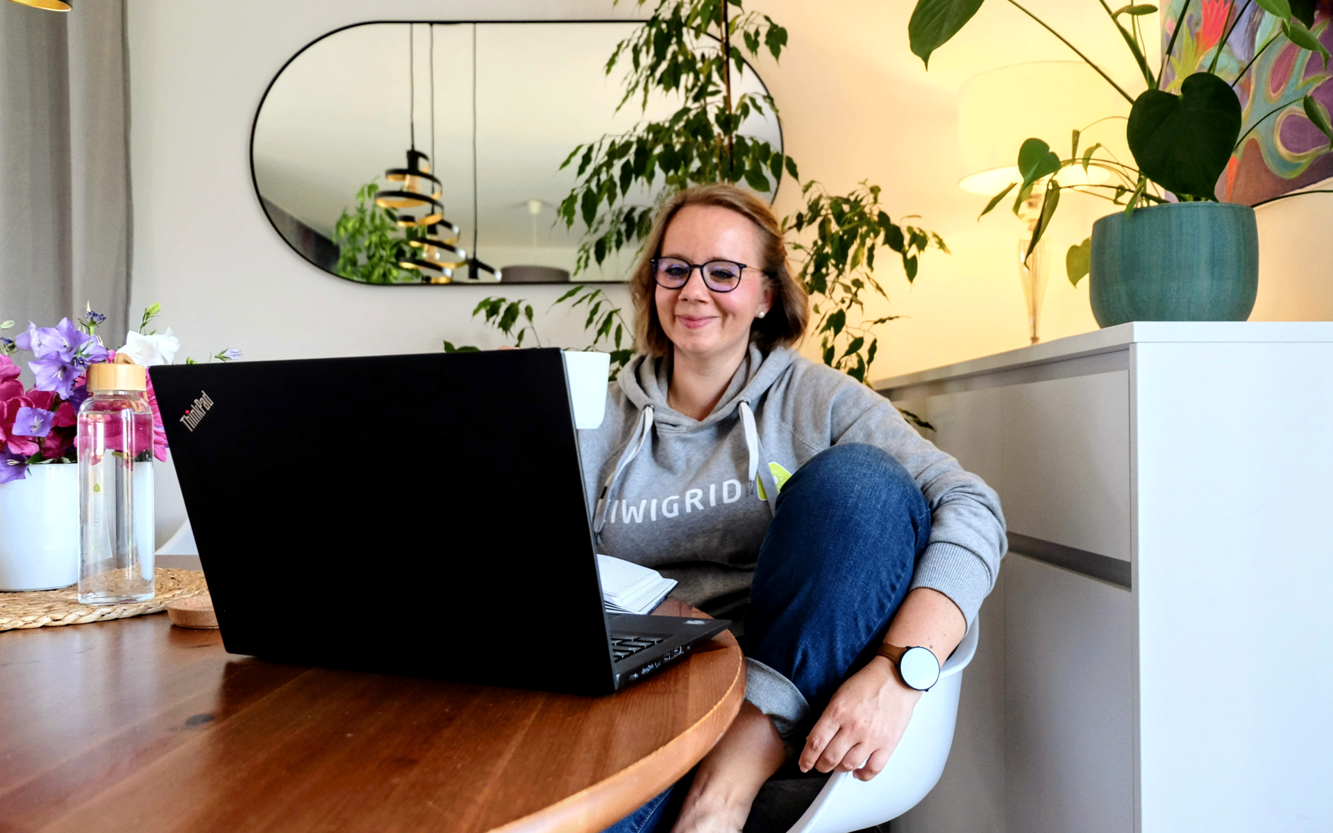 Woman in Kiwigrid hoodie sitting casually in front of a laptop in an apartment.